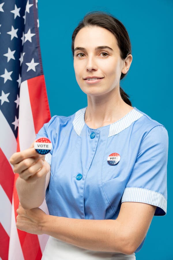 Jeune femme de chambre contemporaine en uniforme bleu montrant les insignes de vote images stock
