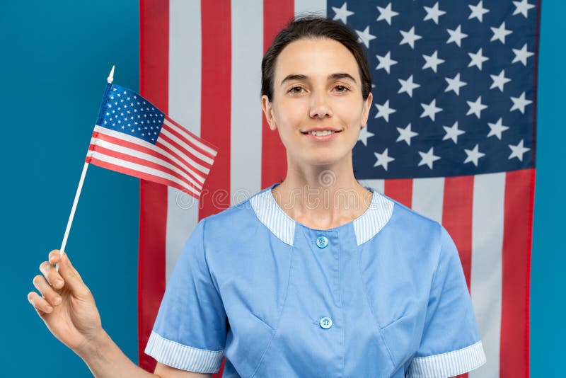 Jeune femme de chambre heureuse brune en uniforme bleu tenant le petit drapeau américain images stock