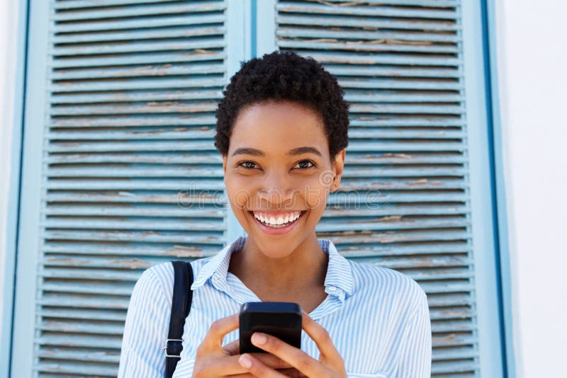 Jeune femme de couleur attirante tenant le téléphone portable photo stock Jeune femme de couleur attirante tenant le téléphone portable photo stock