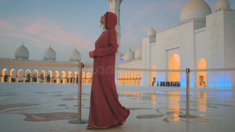 Jeune femme de tourisme dans la longue robe traditionnelle musulmane rose Abaya admire le monument arabe Abu Dhabi banque de vidéos
