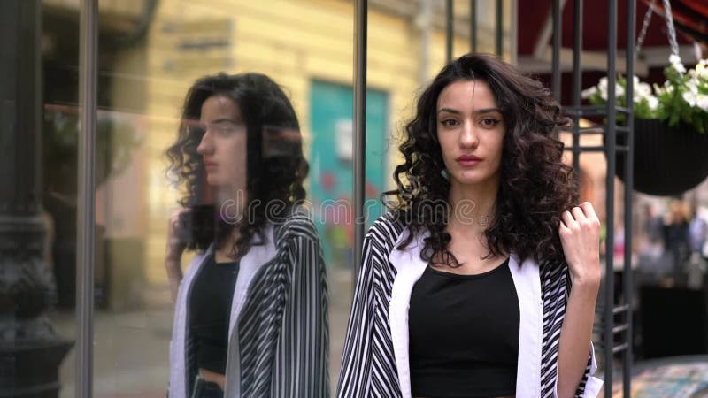 Jeune femme debout à la fenêtre du magasin dans la rue réfléchie dans le verre. beau clips vidéos