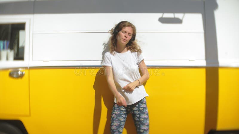 Jeune femme dehors par la musique de écoute de voiture jaune de chariot dans des écouteurs utilisant le smartphone - détente, app banque de vidéos