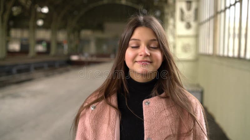 Jeune femme en manteau rose se tient souriant sur la plate-forme de la gare. attente clips vidéos