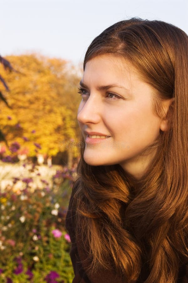 Head portrait of a redhair young woman in autumn park; trees and flowers colored in vivid fall colors. Head portrait of a redhair young woman in autumn park; trees and flowers colored in vivid fall colors