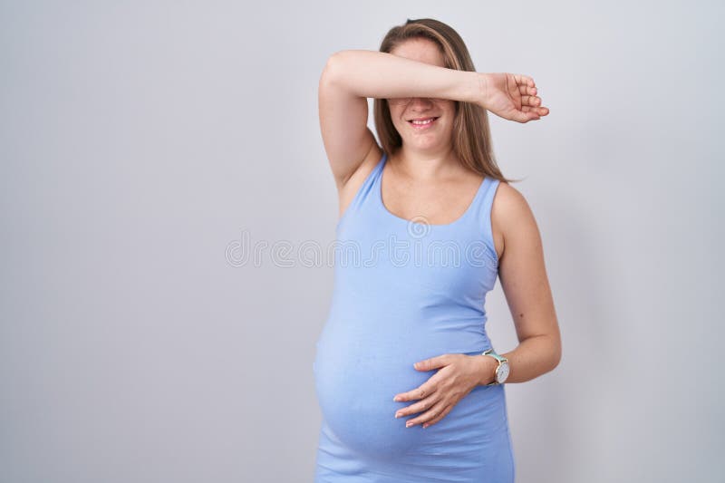 Jeune femme enceinte debout sur fond blanc souriant joyeux en jouant à peek a boo avec les mains montrant visage photo libre de droits