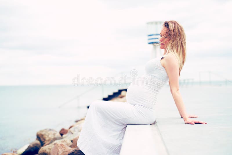 Jeune femme enceinte détendant au bord de la mer photographie stock libre de droits Jeune femme enceinte détendant au bord de la mer photographie stock libre de droits