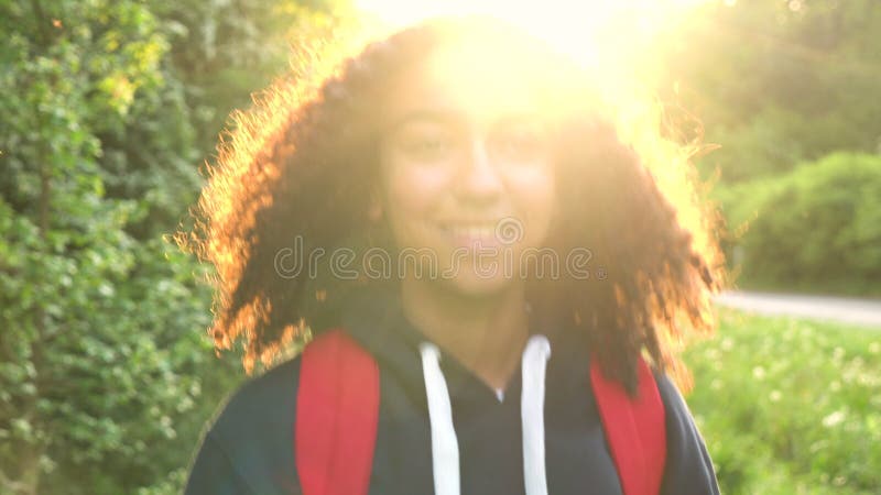Jeune femme féminine de belle de métis d'Afro-américain adolescente heureuse de fille trimardant avec le sac à dos rouge dans le banque de vidéos