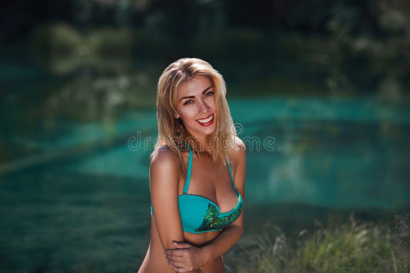 Jeune femme gaie dans les vêtements de bain se reposant près du lac photo libre de droits Jeune femme gaie dans les vêtements de bain se reposant près du lac photo libre de droits