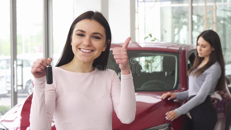 Jeune femme gaie montrant des pouces tenant des clés de voiture image libre de droits Jeune femme gaie montrant des pouces tenant des clés de voiture image libre de droits