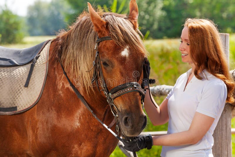 Jeune femme heureuse alimentant son beau cheval de baie photo stock Jeune femme heureuse alimentant son beau cheval de baie photo stock