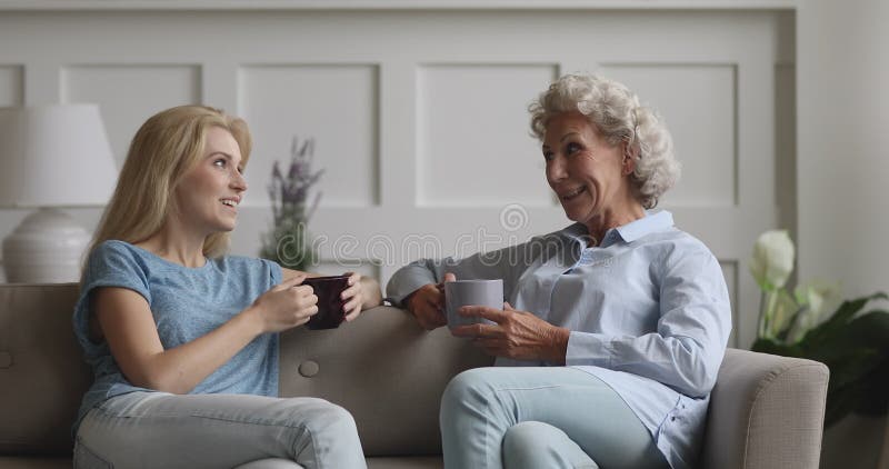 Jeune femme heureuse assise sur le divan causant avec une mère âgée. clips vidéos