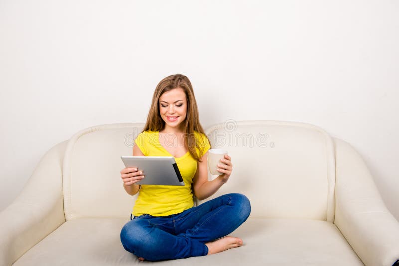 Jeune femme heureuse avec une tasse tenant une tablette assise sur le canapé photographie stock