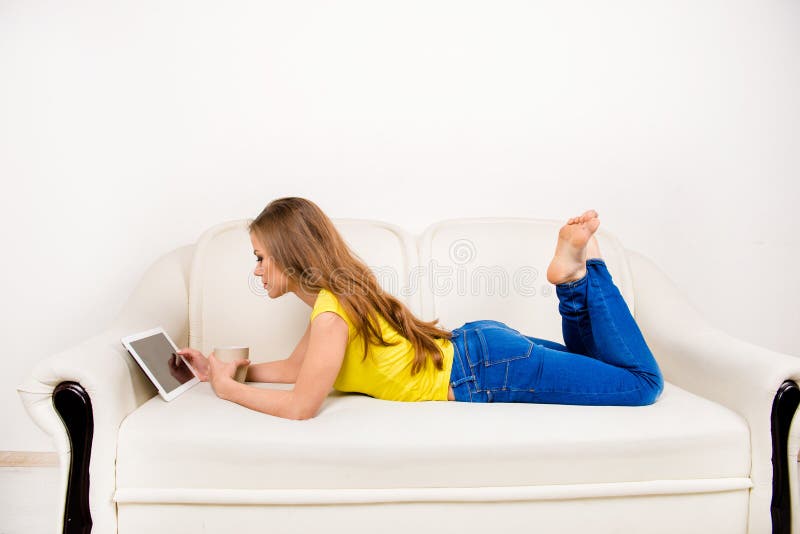 Jeune femme heureuse avec une tasse tenant une tablette posée sur le canapé photo libre de droits
