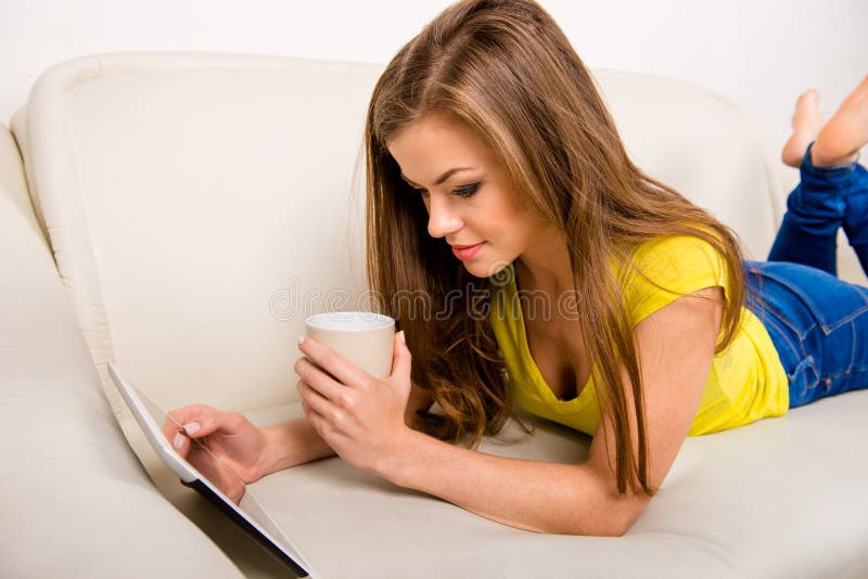 Jeune femme heureuse avec une tasse tenant une tablette posée sur le canapé images libres de droits