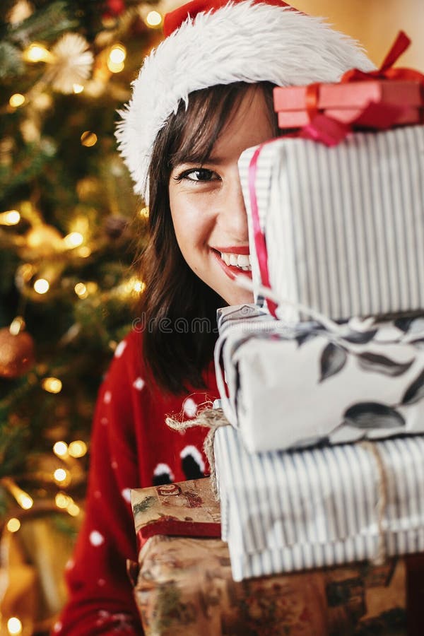 Jeune femme heureuse dans le chapeau de Santa tenant la pile des boîte-cadeau au gol photographie stock libre de droits Jeune femme heureuse dans le chapeau de Santa tenant la pile des boîte-cadeau au gol photographie stock libre de droits