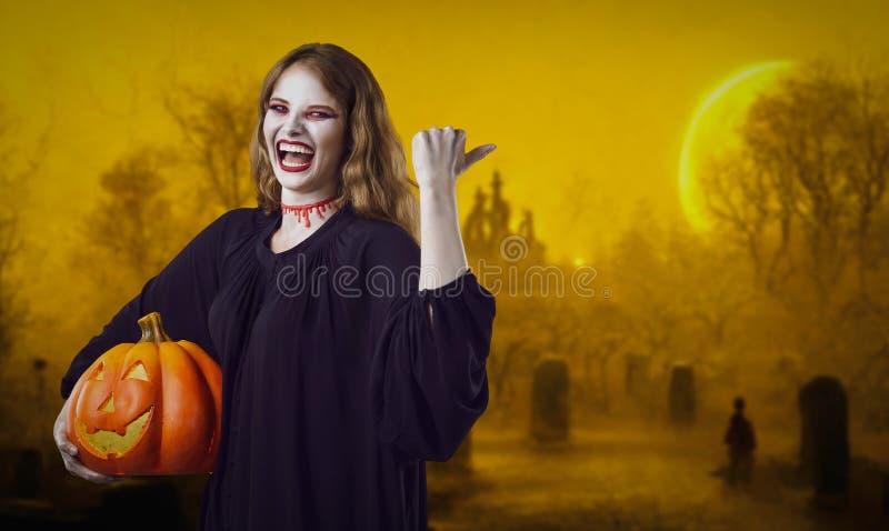 Happy witch showing something on graveyard background. Young woman in Halloween costume with crazy excited face expression laughing and pointing at mysterious yellow foggy misty cemetery backdrop. Happy witch showing something on graveyard background. Young woman in Halloween costume with crazy excited face expression laughing and pointing at mysterious yellow foggy misty cemetery backdrop