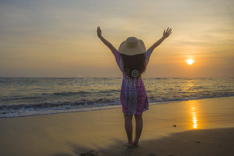 Jeune femme heureuse et décontractée dans le chapeau d'été regardant le soleil au-dessus de la mer pendant un beau coucher du sol photo libre de droits Jeune femme heureuse et décontractée dans le chapeau d'été regardant le soleil au-dessus de la mer pendant un beau coucher du sol photo libre de droits