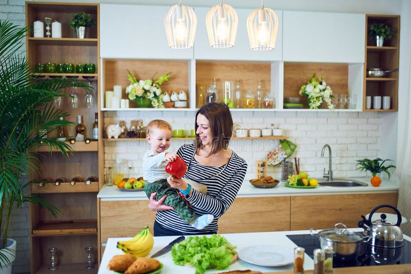 Jeune femme heureuse tenant un enfant de 1 an et faisant cuire ensemble dans la cuisine photos libres de droits Jeune femme heureuse tenant un enfant de 1 an et faisant cuire ensemble dans la cuisine photos libres de droits