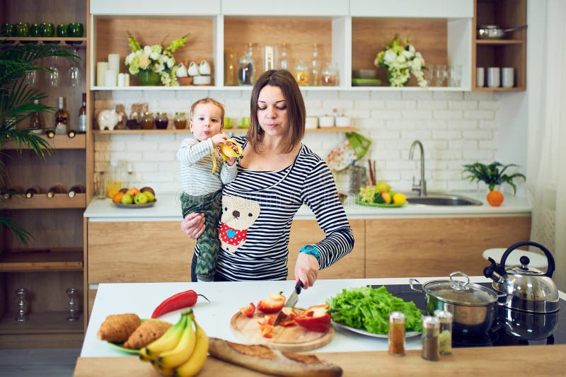 Jeune femme heureuse tenant un enfant de 1 an et faisant cuire ensemble dans la cuisine photos stock Jeune femme heureuse tenant un enfant de 1 an et faisant cuire ensemble dans la cuisine photos stock