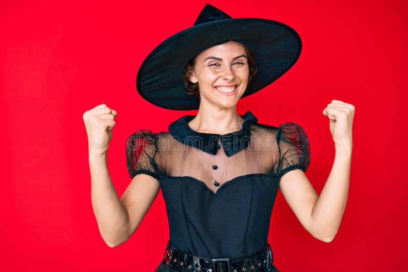 Young hispanic woman wearing witch halloween costume screaming proud, celebrating victory and success very excited with raised arms. Young hispanic woman wearing witch halloween costume screaming proud, celebrating victory and success very excited with raised arms