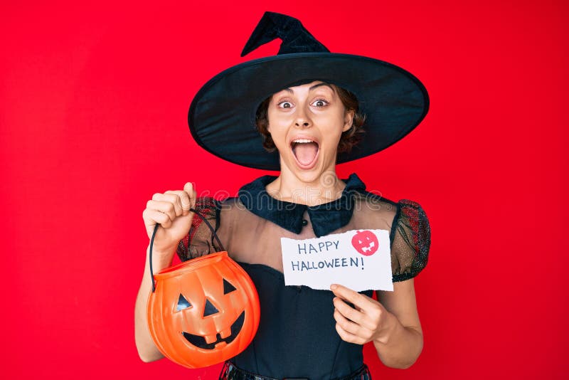 Young hispanic woman wearing witch costume holding pumpkin and happy halloween message celebrating crazy and amazed for success with open eyes screaming excited. Young hispanic woman wearing witch costume holding pumpkin and happy halloween message celebrating crazy and amazed for success with open eyes screaming excited