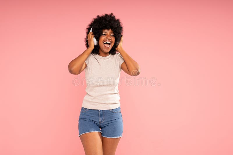 Jeune femme joyeuse avec coiffure afro danser écouter de la musique dans les écouteurs s'amuser seule. fille heureuse images stock
