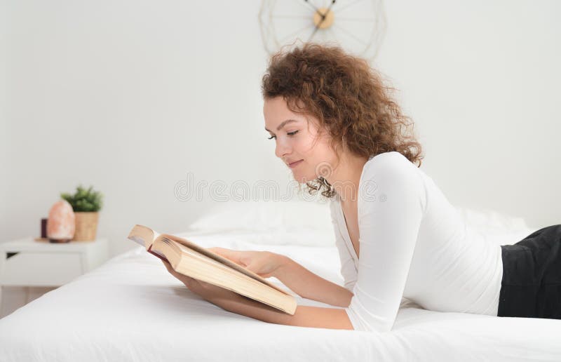 Jeune femme lisant un livre sur le lit pendant le matin photo libre de droits Jeune femme lisant un livre sur le lit pendant le matin photo libre de droits