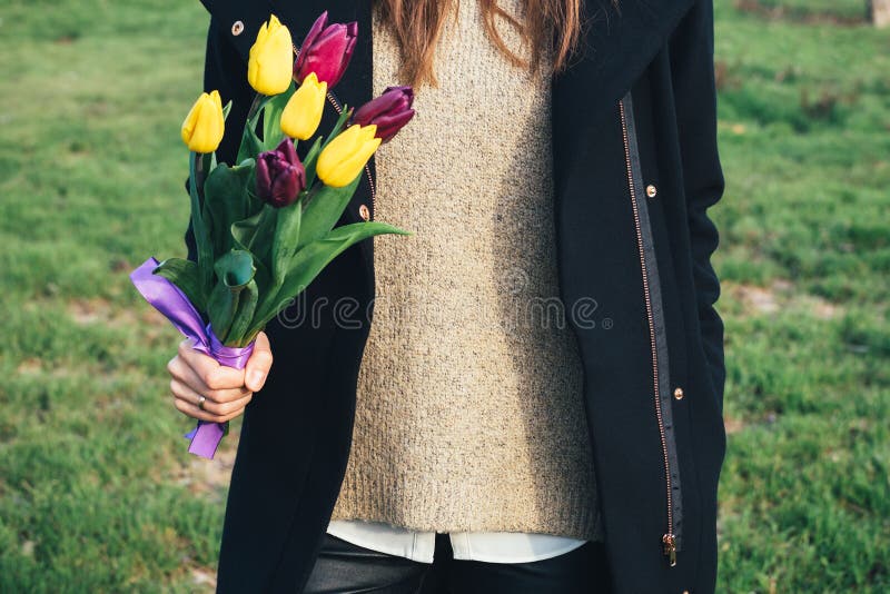 Jeune femme mince dans le manteau se tenant sur l'herbe verte et tenant un b photo stock Jeune femme mince dans le manteau se tenant sur l'herbe verte et tenant un b photo stock