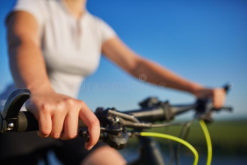 Jeune femme mince s'asseyant sur la bicyclette, tenant des guidons avec des mains Femme dans l'éclairage de coucher du soleil de photos stock Jeune femme mince s'asseyant sur la bicyclette, tenant des guidons avec des mains Femme dans l'éclairage de coucher du soleil de photos stock