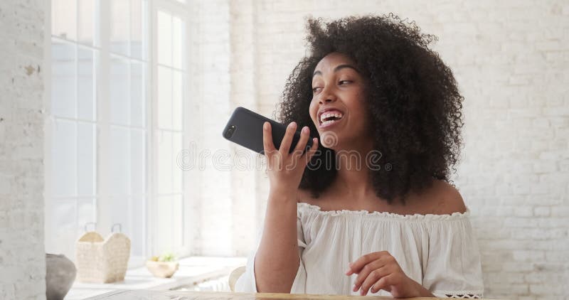 Jeune femme mixte enregistrant un message audio à un ami à l'aide d'un smartphone assis à la table à la maison fermer la vue. banque de vidéos