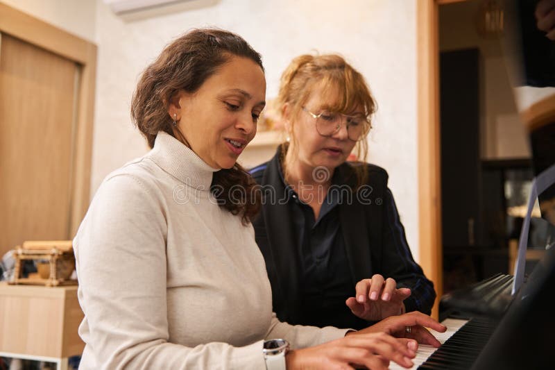Jeune femme multi-ethnique adulte apprenant à jouer au pianoforte avec son enseignant intérieur image libre de droits