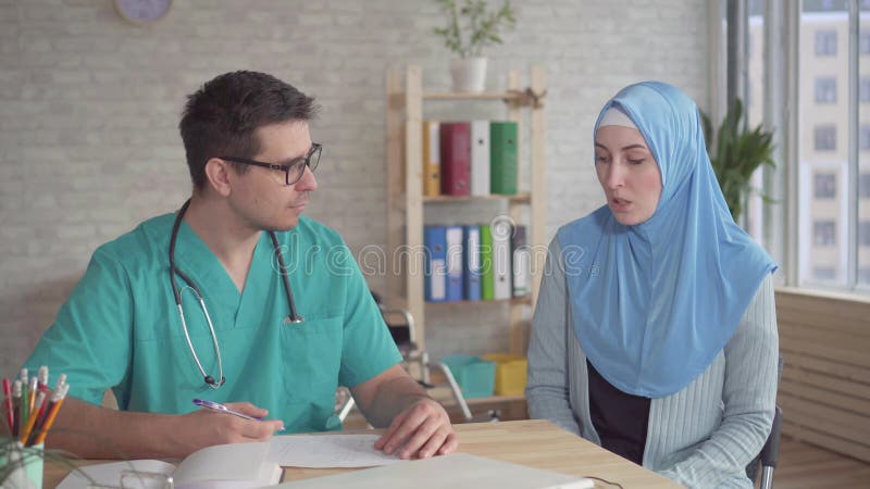 Jeune femme musulmane de portrait dans le hijab aux hommes du rendez-vous d'un docteur banque de vidéos