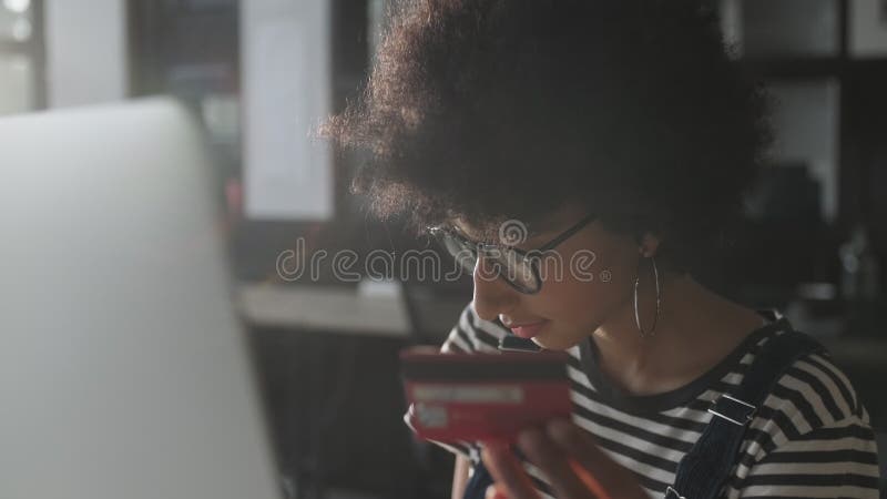 Jeune femme métisse acheter en ligne avec la carte de crédit à l'aide de l'ordinateur portable pour siéger à l'intérieur. Achats à banque de vidéos