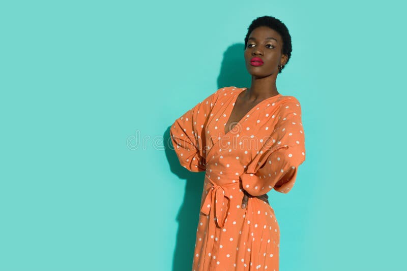 Jeune femme noire confiante posant en robe de pois orange photographie stock libre de droits