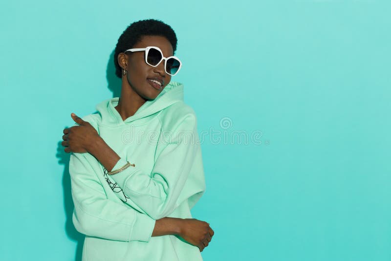 Jeune femme noire joyeuse en sweat-shirt turquoise pastel et lunettes de soleil blanches images libres de droits