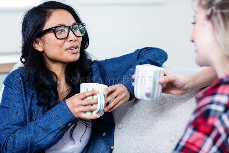 Close-up of young women talking with female friend while drinking coffee at home. Close-up of young women talking with female friend while drinking coffee at home
