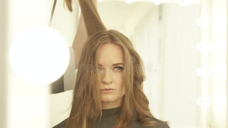 Jeune femme pendant le séchage de longs cheveux avec le dessiccateur et le miroir avant de brosse à cheveux dans le salon de coif banque de vidéos