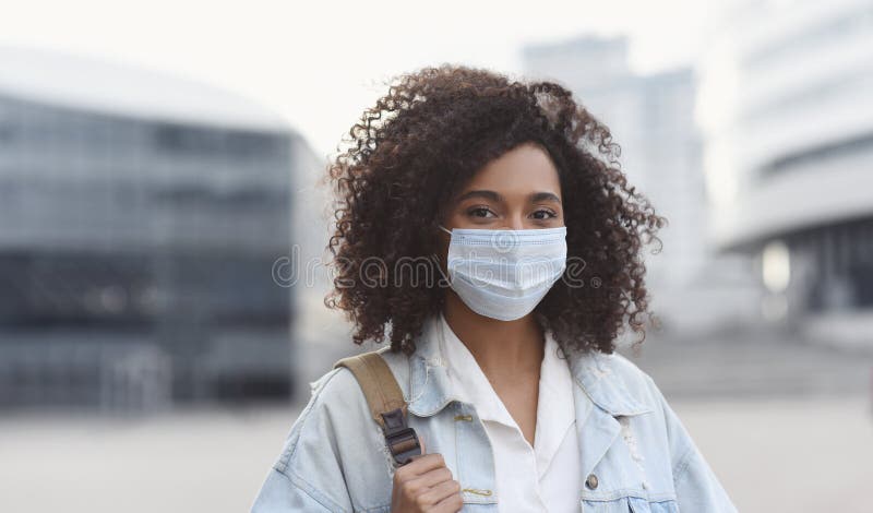 Young woman wearing protective face mask in a city. Masked african-american teenage student girl on a city street. Epidemic, pandemic, corona virus protection, healthy lifestyle, people concept. Young woman wearing protective face mask in a city. Masked african-american teenage student girl on a city street. Epidemic, pandemic, corona virus protection, healthy lifestyle, people concept