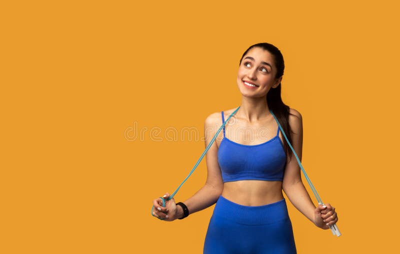 Jeune femme posant avec la corde de saut au studio orange images stock