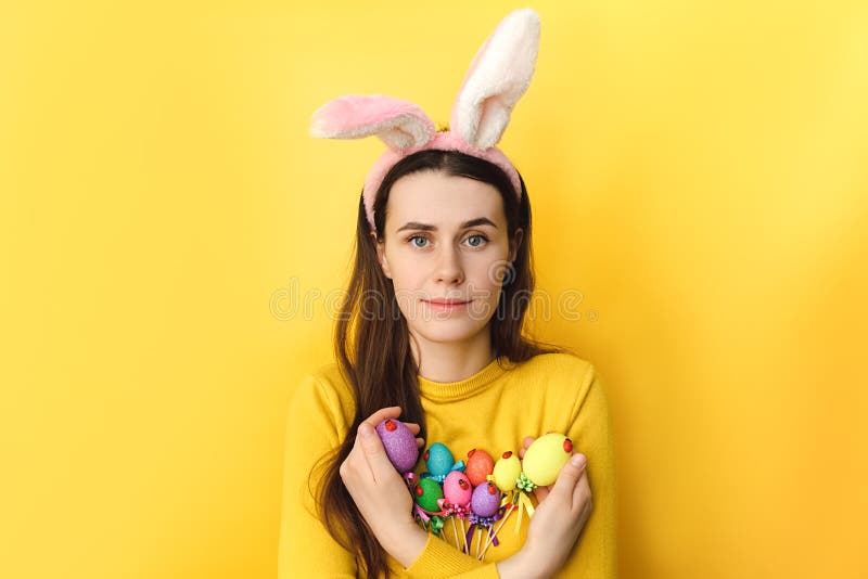Jeune femme positive porte des oreilles moelleuses tient des oeufs colorés sur les bâtons étant en bonne humeur après la peinture image stock