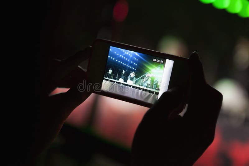 Jeune femme prenant une photographie avec son téléphone intelligent à un concert d'intérieur, plan rapproché sur des mains photos stock Jeune femme prenant une photographie avec son téléphone intelligent à un concert d'intérieur, plan rapproché sur des mains photos stock
