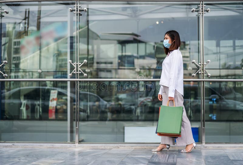 Young asian woman walking and holding shopping bag in front of store and his wearing medical mask for prevention from coronavirus Covid-19 pandemic. new normal concepts. Young asian woman walking and holding shopping bag in front of store and his wearing medical mask for prevention from coronavirus Covid-19 pandemic. new normal concepts