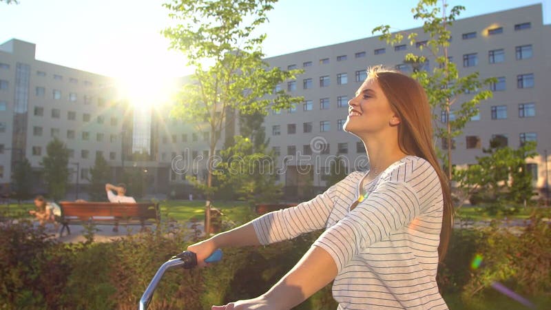 Jeune femme romantique heureuse faisant un cycle heureusement par une rue ensoleillée dans l'été dehors Bicyclette d'équitation d clips vidéos