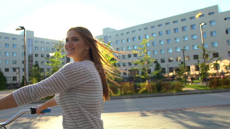 Jeune femme romantique heureuse faisant un cycle heureusement par une rue ensoleillée dans l'été dehors Bicyclette d'équitation d banque de vidéos