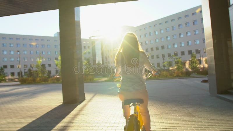 Jeune femme romantique heureuse faisant un cycle heureusement par une rue ensoleillée dans l'été dehors Bicyclette d'équitation d banque de vidéos
