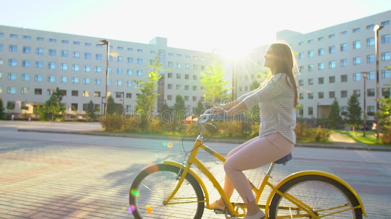 Jeune femme romantique heureuse faisant un cycle heureusement par une rue ensoleillée dans l'été dehors Bicyclette d'équitation d banque de vidéos