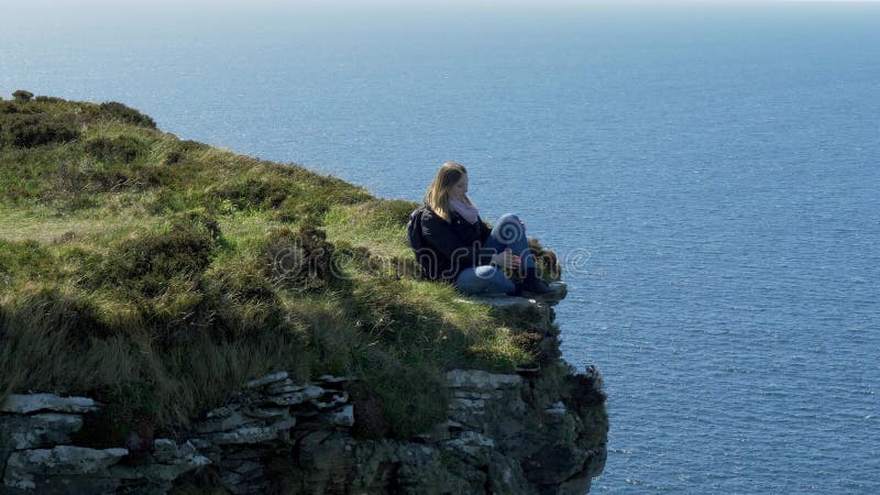 Jeune femme s'asseyant au bord d'une falaise à la côte ouest irlandaise