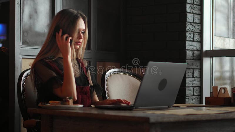Jeune femme s'asseyant dans le café à la table en bois, café potable et à l'aide du smartphone Sur la table est l'ordinateur port