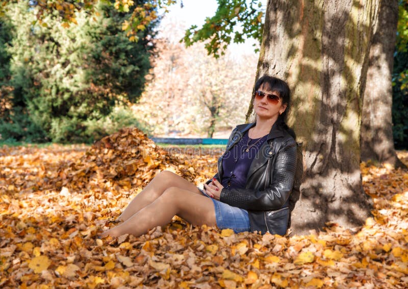 Jeune femme s'asseyant sur l'herbe en parc en automne photo libre de droits Jeune femme s'asseyant sur l'herbe en parc en automne photo libre de droits