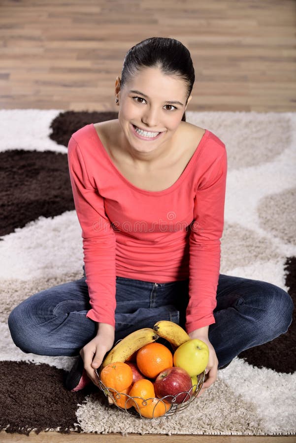 Jeune femme s'asseyant sur le tapis et appréciant des fruits image libre de droits Jeune femme s'asseyant sur le tapis et appréciant des fruits image libre de droits